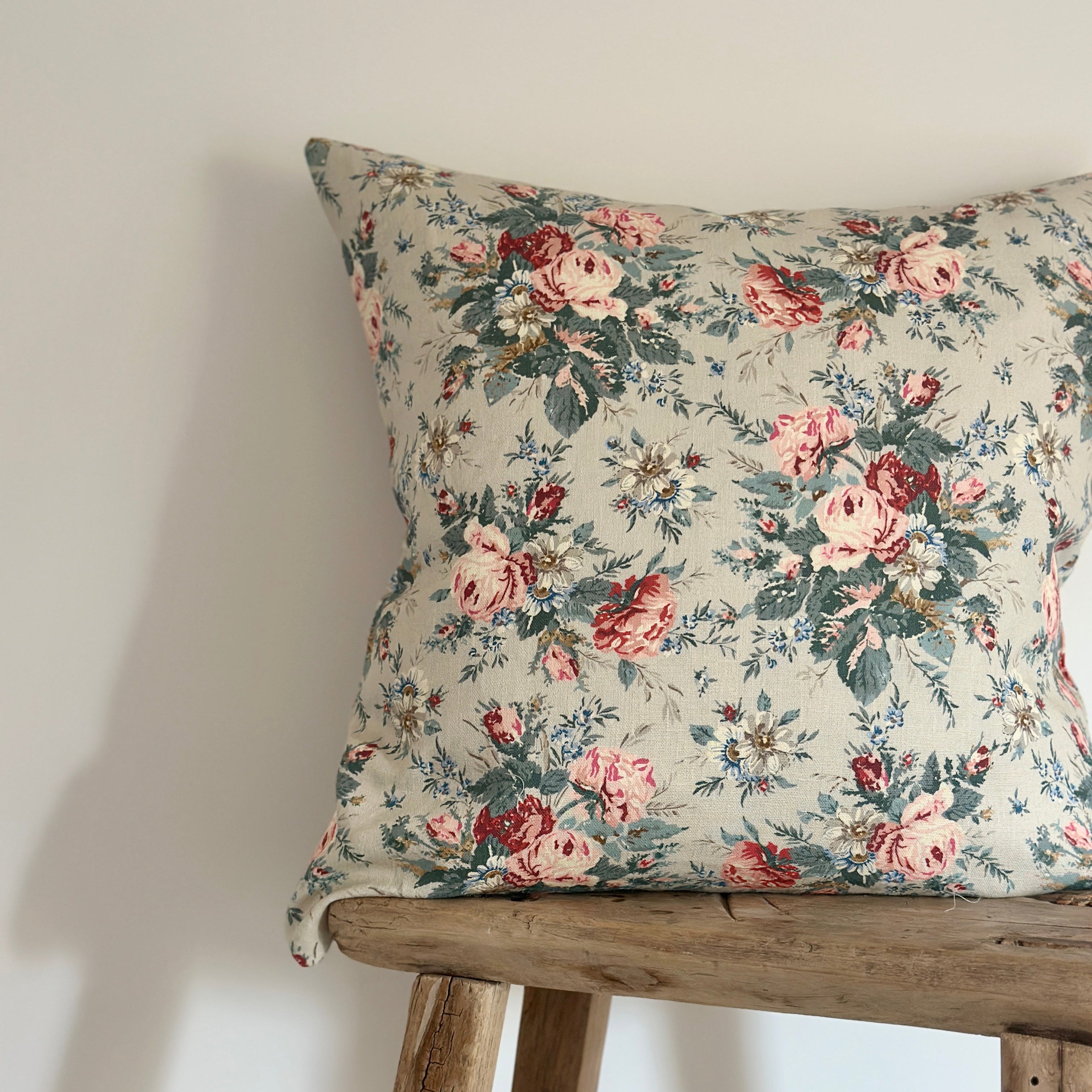 A square throw pillow with a vintage floral print in pink, red, and green on a cream background.