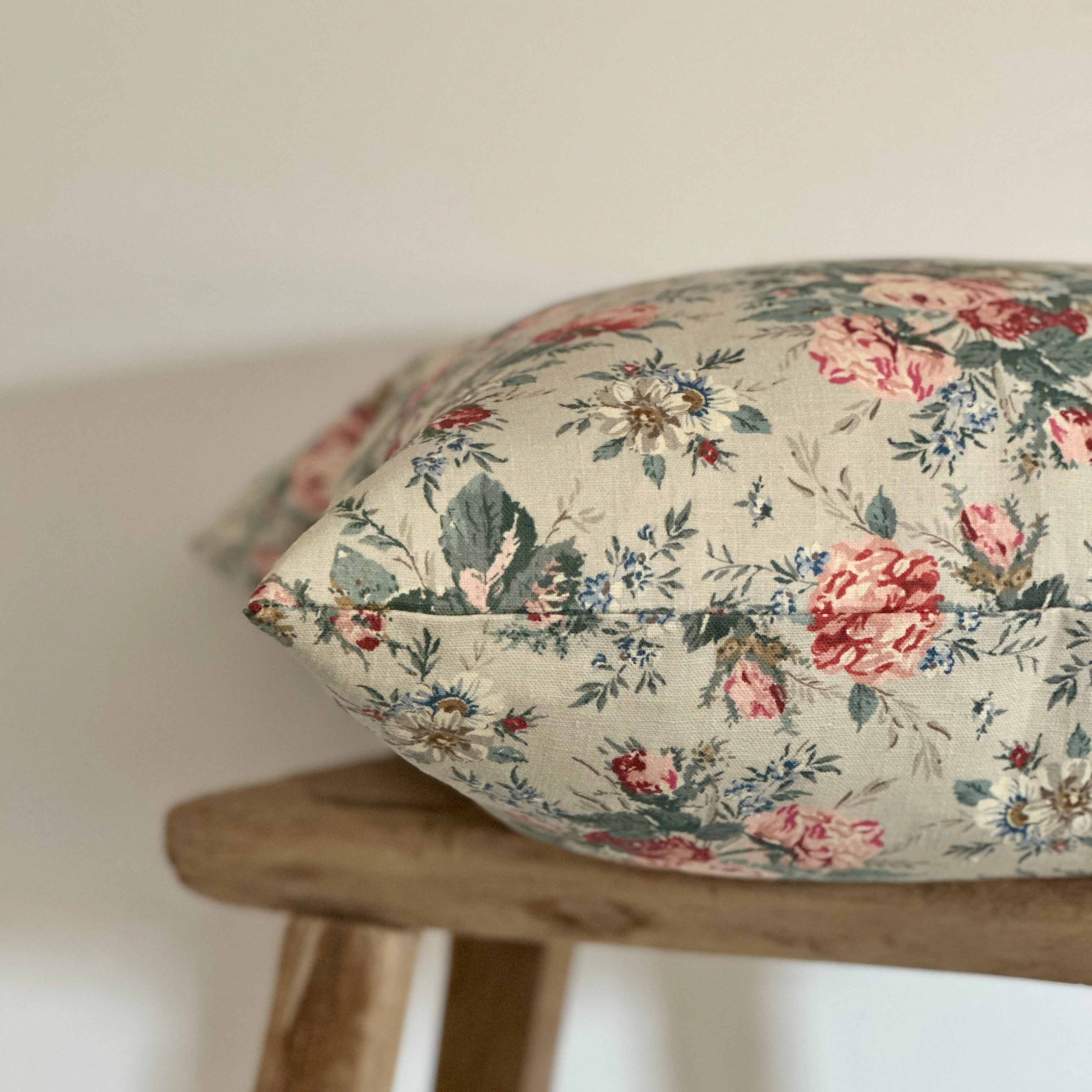 A floral cushion with a vintage rose pattern in pink, green, and beige.