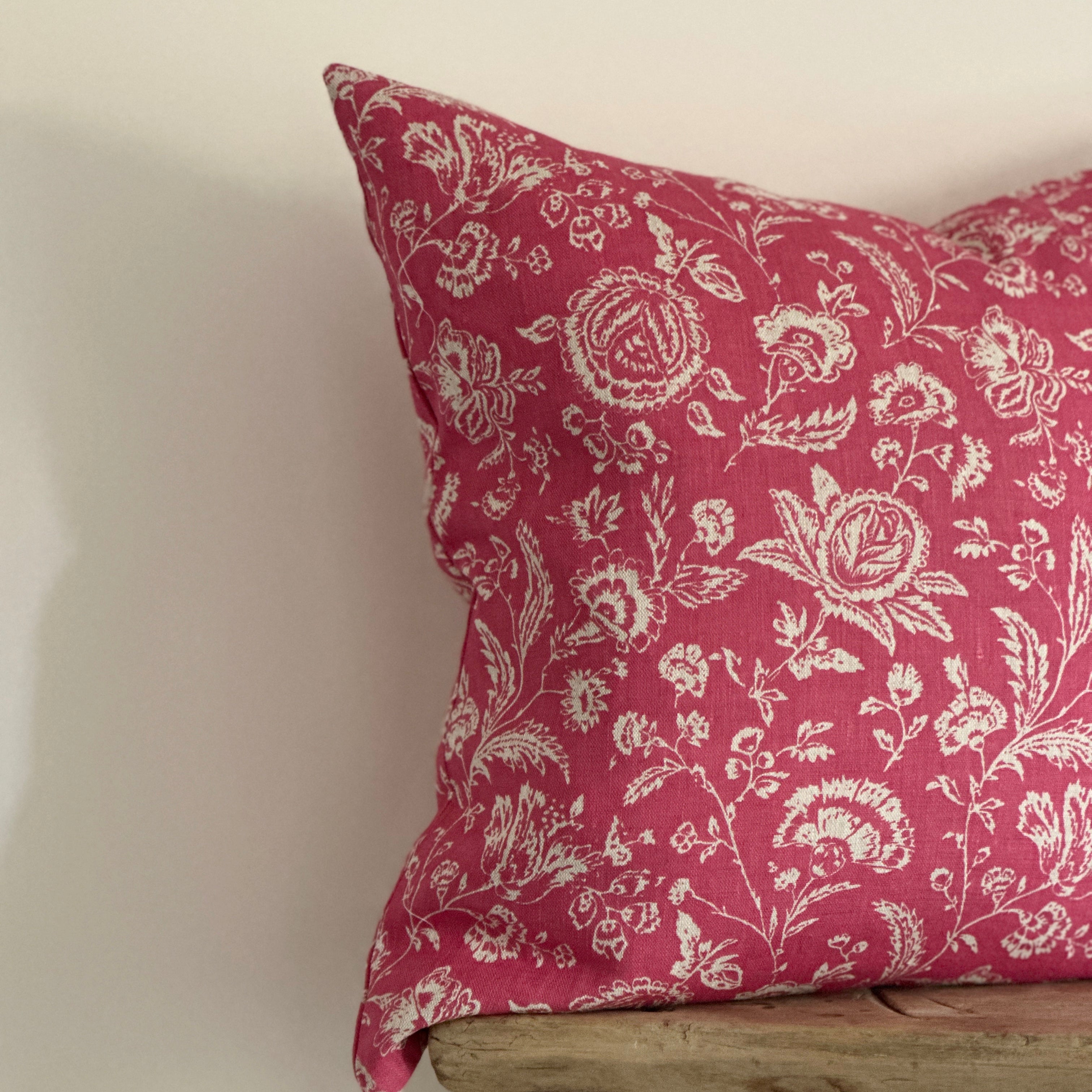 A square decorative cushion with a red and cream floral toile pattern.